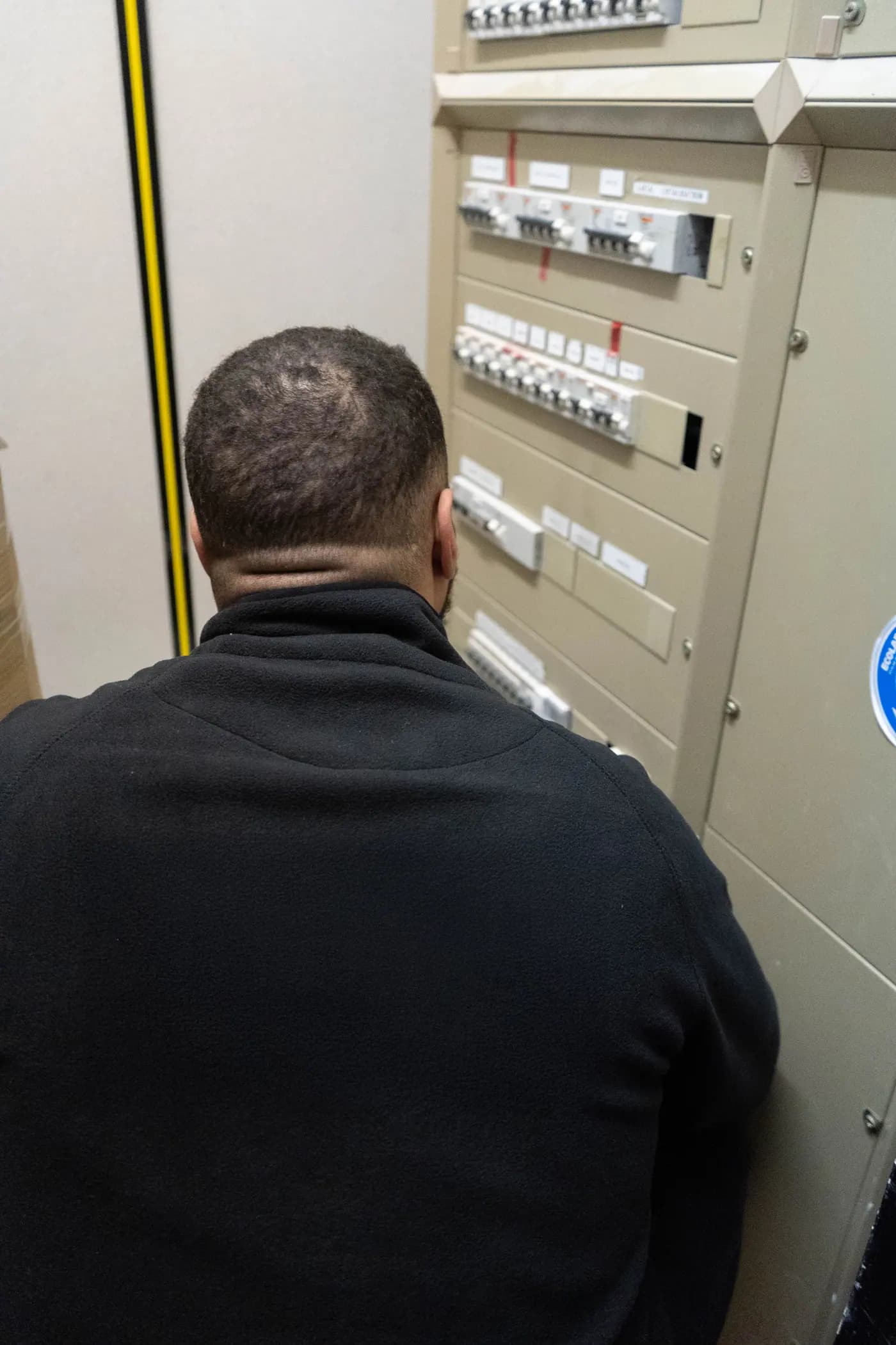 Électricien intervenant sur un tableau de distribution électrique dans un local technique d'immeuble