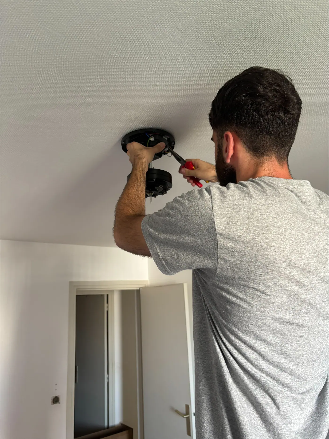 Électricien raccordant un point lumineux au plafond d'un logement